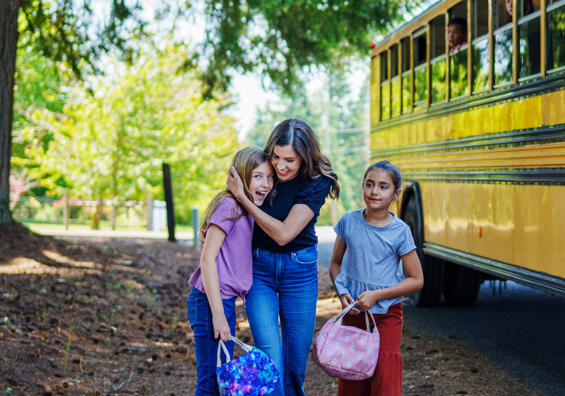 woman hugging girl in front of school bus